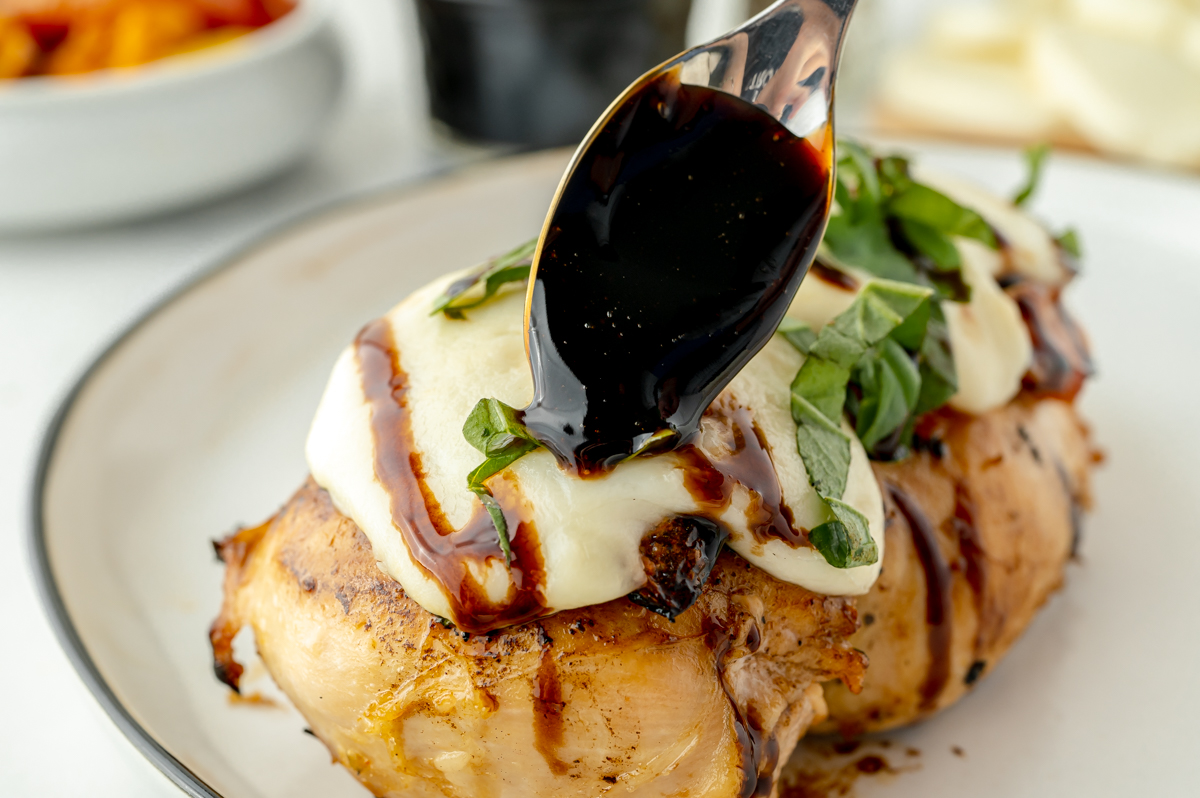 spoon adding balsamic reduction sauce to chicken