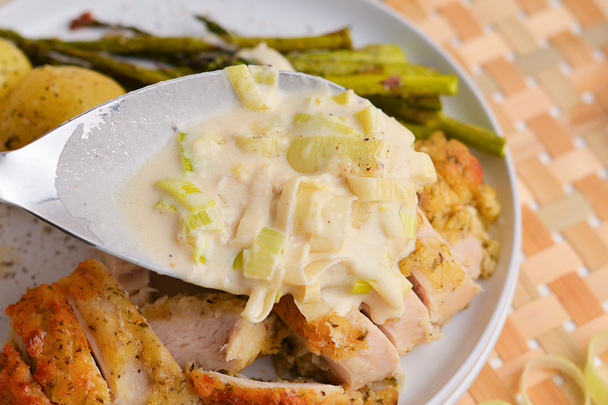 close up of creamy leek sauce pouring over sliced chicken