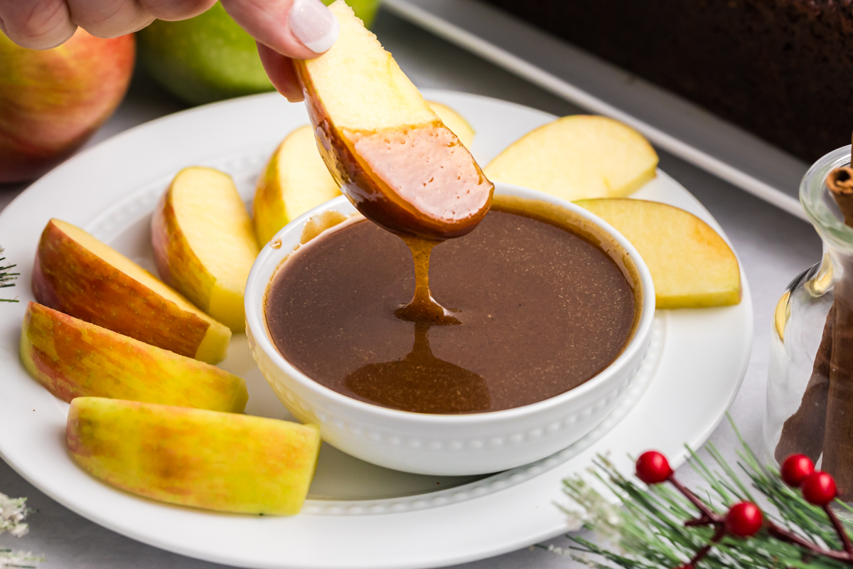 hand dipping apple slice into gingerbread caramel sauce