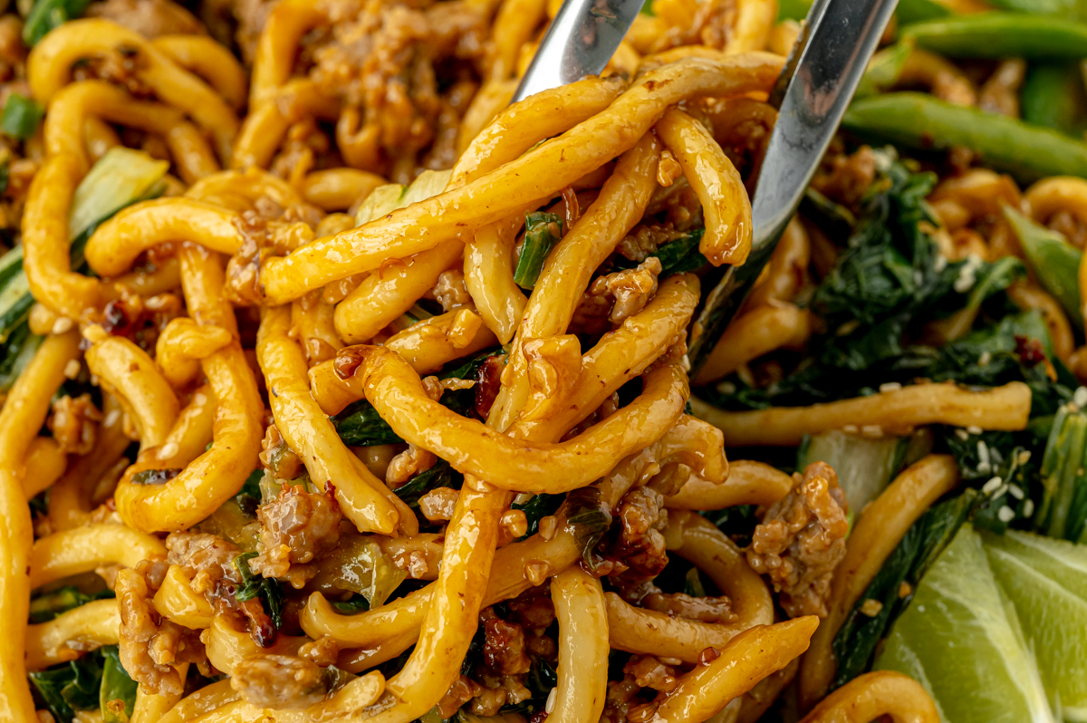 close up shot of noodles tossed in sauce held by tongs