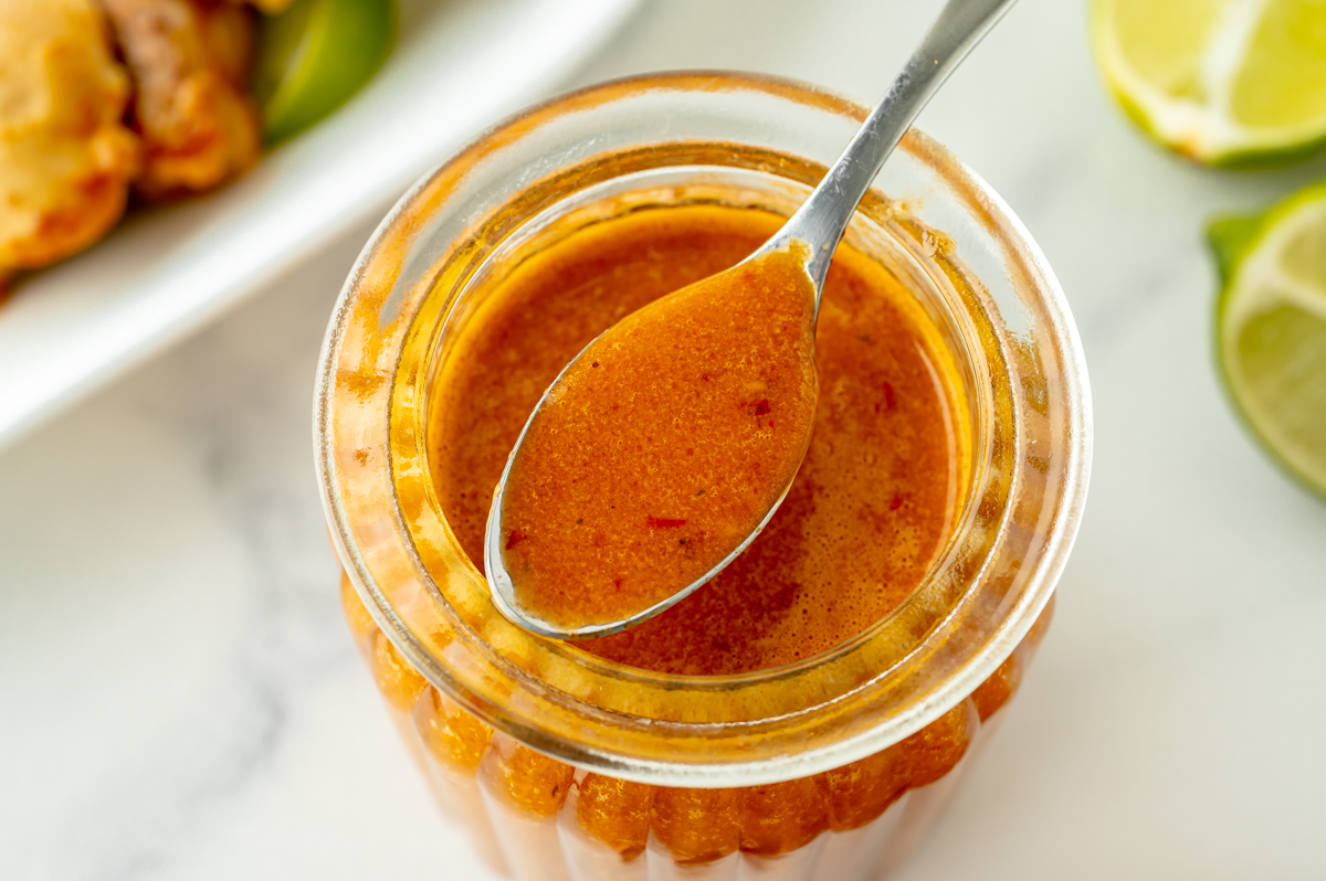 angled shot of orange sauce in spoon over jar