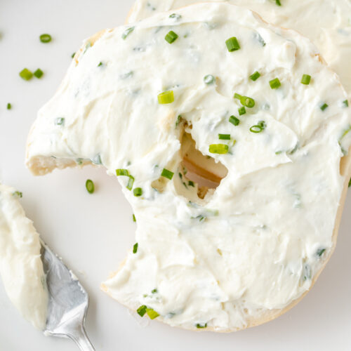 bite taken out of bagel topped with chive and onion cream cheese