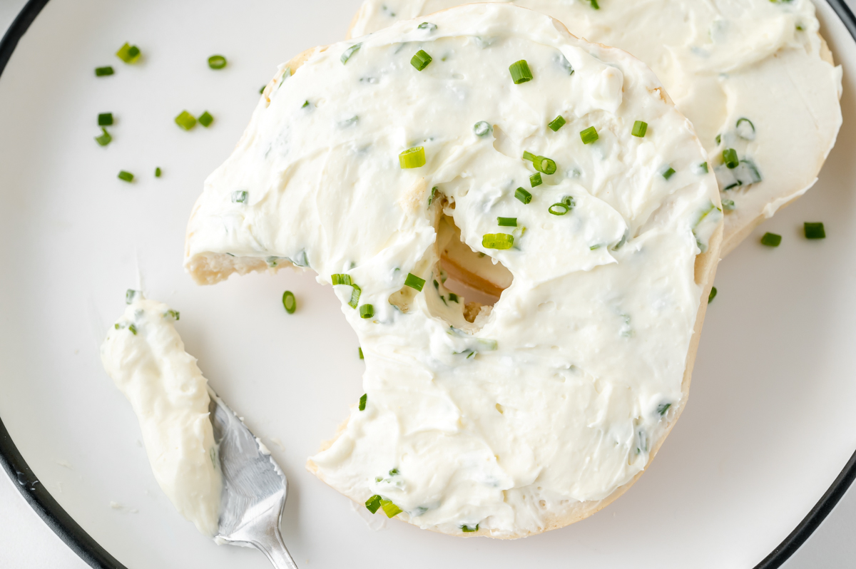 bite taken out of bagel topped with chive and onion cream cheese