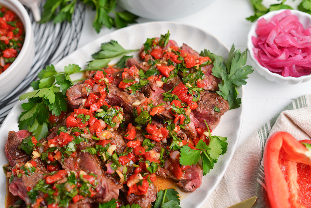 platter of steak topped with sauce and cilantro